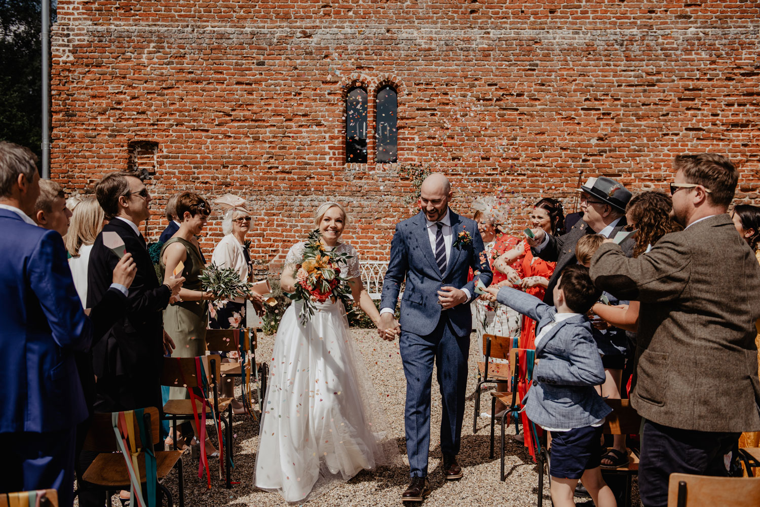 abbey hall eye suffolk wedding smiling bride walking down the aisle carrying a pink peony bouquet by anne schwarz photography