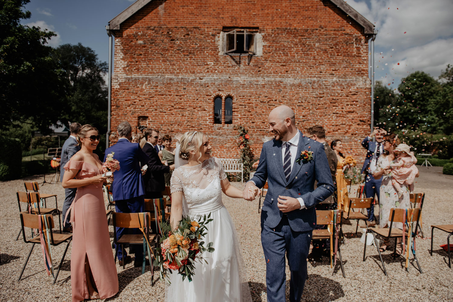 abbey hall eye suffolk wedding smiling bride walking down the aisle carrying a pink peony bouquet by anne schwarz photography