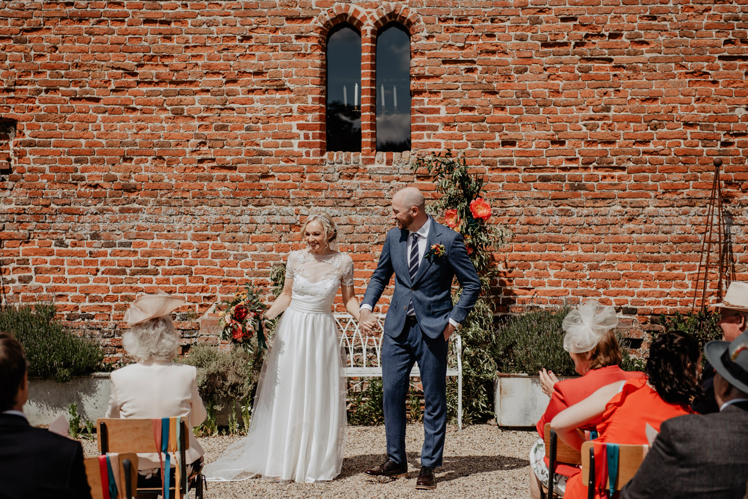 abbey hall eye suffolk wedding smiling bride walking down the aisle carrying a pink peony bouquet by anne schwarz photography