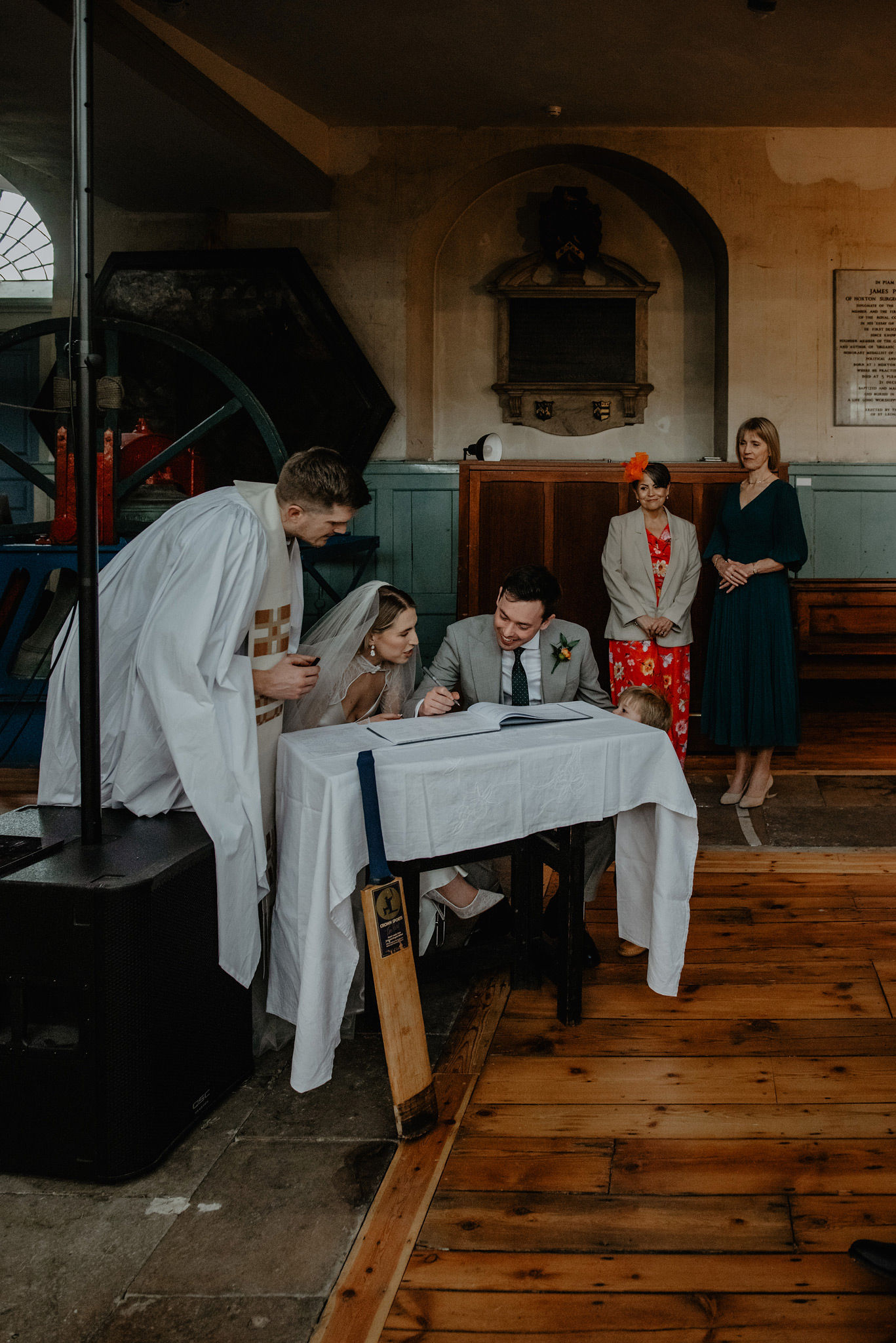 bride and groom signing the wedding register with page boy peeking over the table at shoreditch church st leonards 