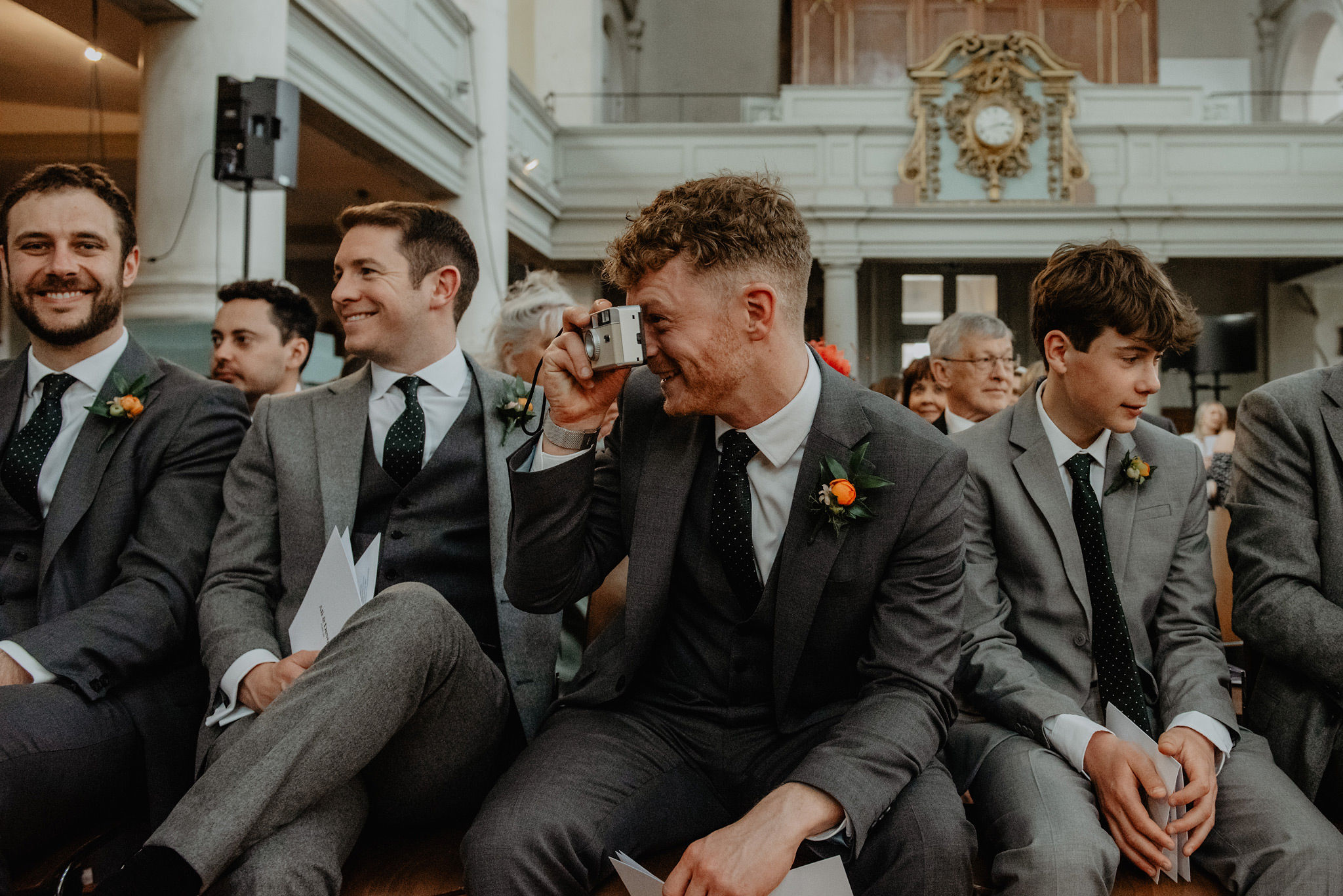 best man in grey suit taing picture on disposal camera at wedding service in shoreditch church