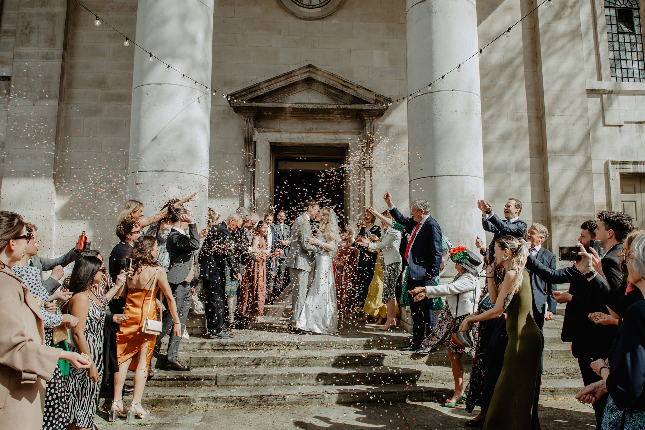 bride and groom kiss with confetti at wedding outside shoreditch church by anne schwarz photography