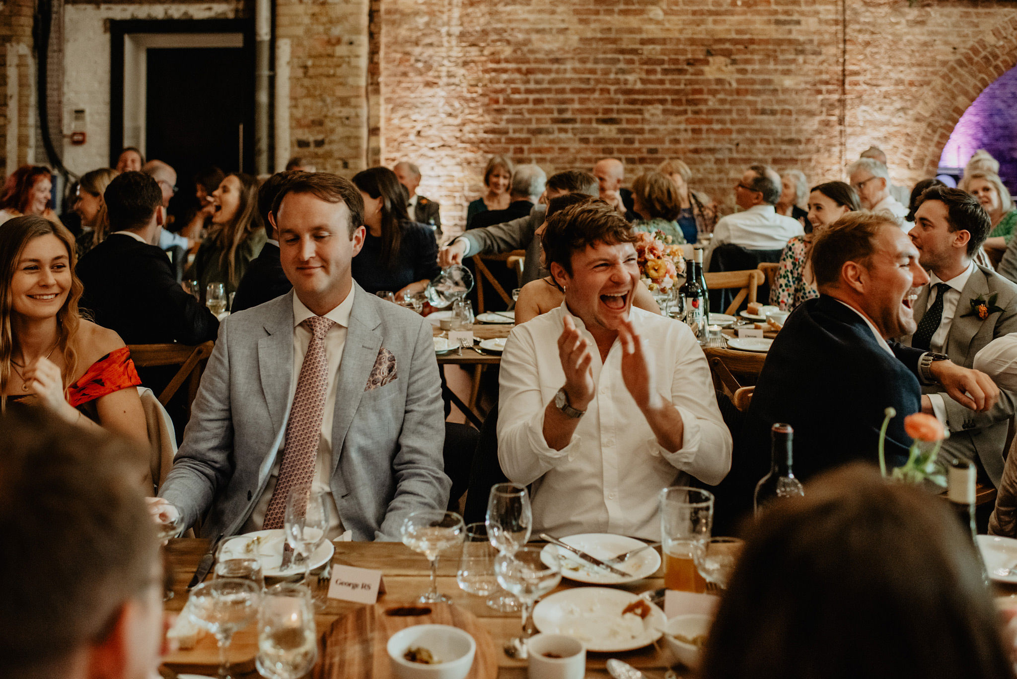 guests laughing during speeches at shoreditch studios wedding photography by anne schwarz